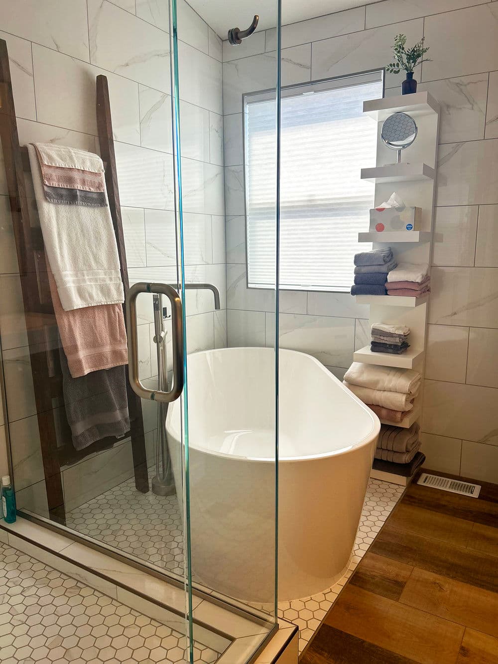 Modern bathroom with glass shower, freestanding tub, and neatly arranged towels on shelves.