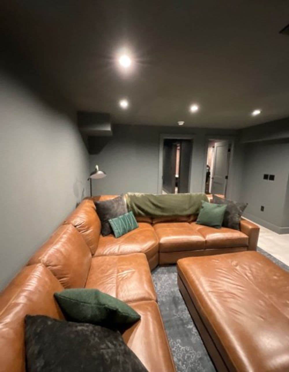 Cozy modern living room with brown leather sectional sofa and green decorative pillows.