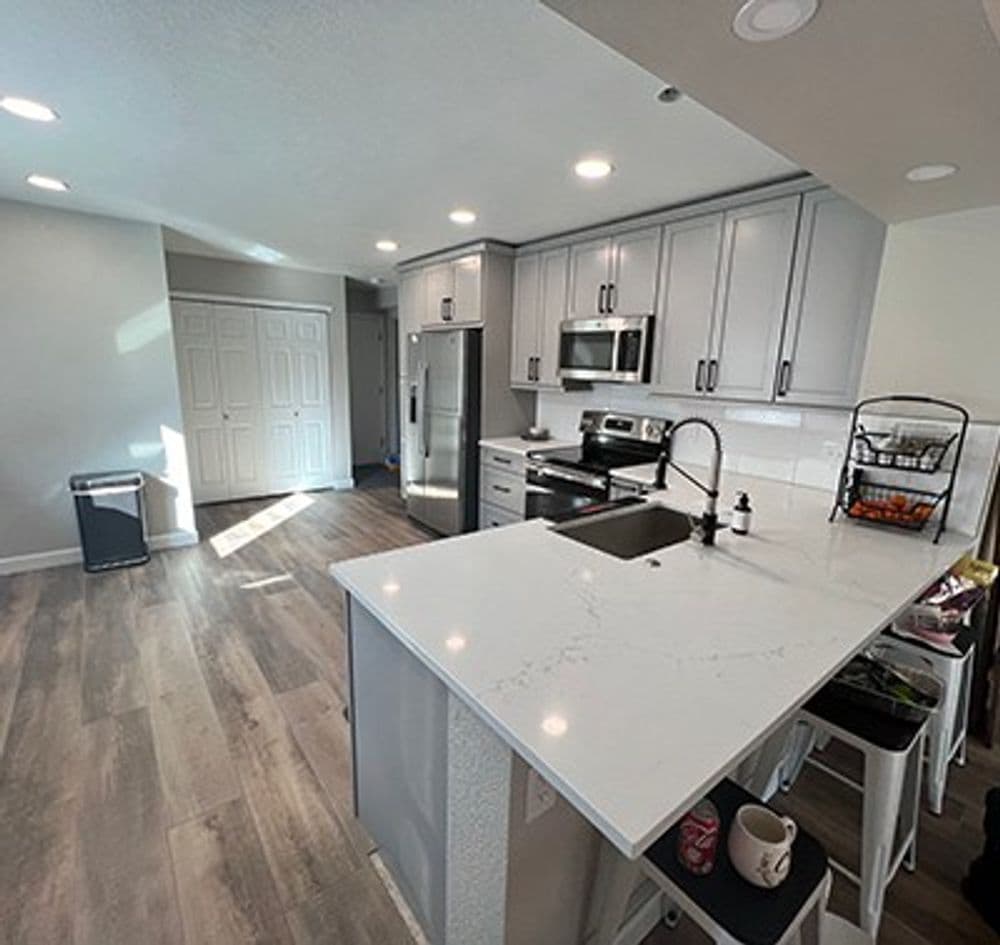 Modern kitchen with gray cabinets, stainless steel appliances, and a sleek white countertop.