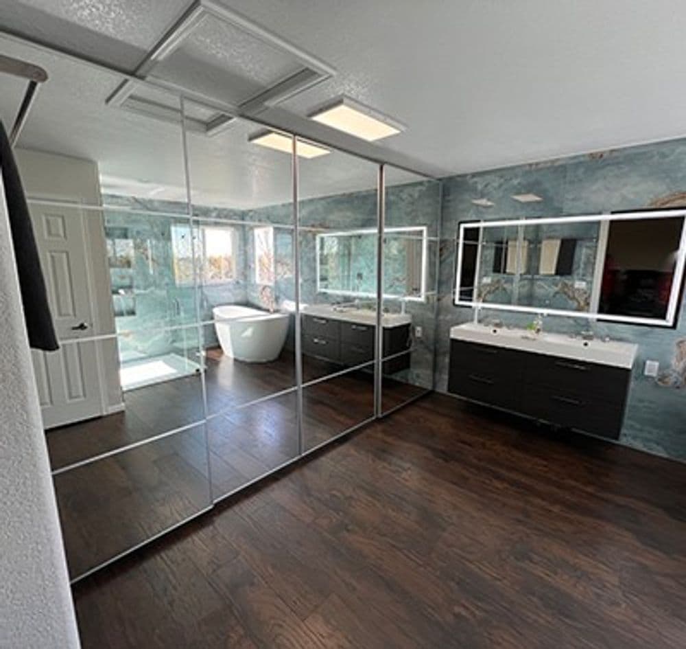 Spacious modern bathroom with mirrored walls, dual vanities, freestanding tub, and wood flooring.