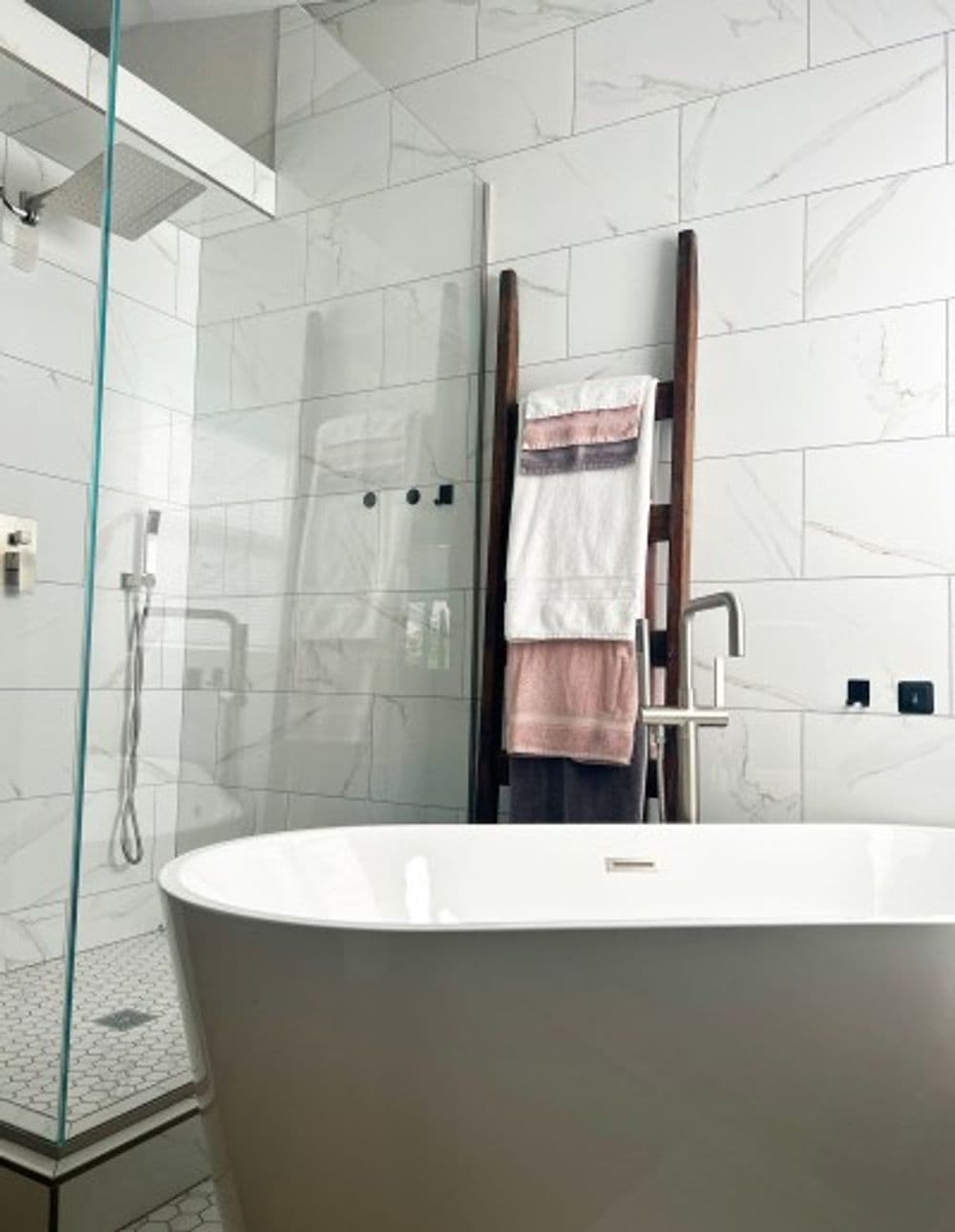 Modern bathroom features a freestanding tub, glass shower, and stylish towel rack.
