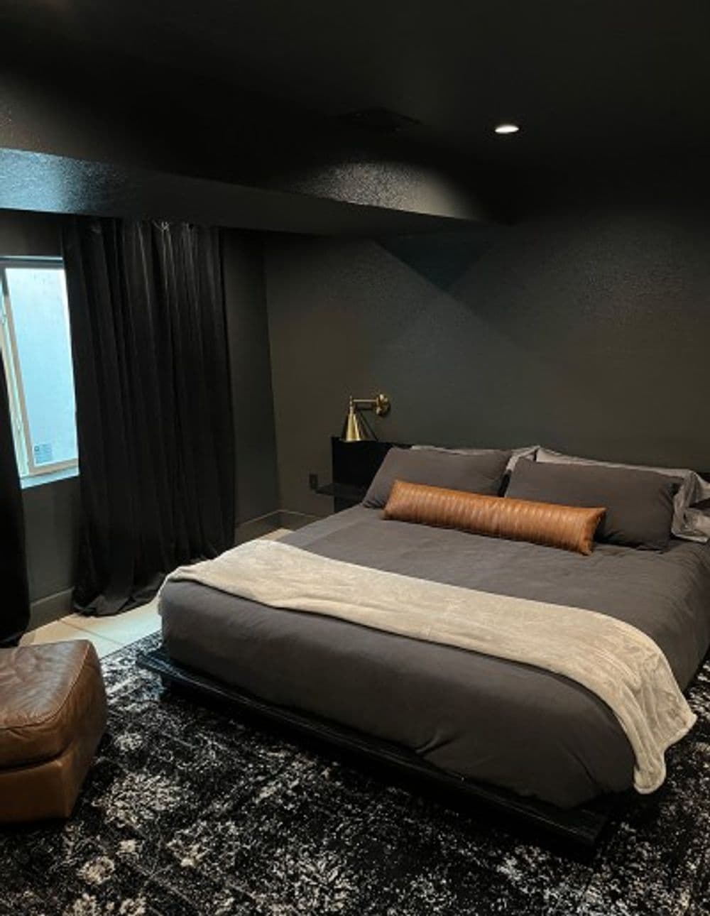 Cozy modern bedroom with dark walls, large bed, and stylish decor elements.