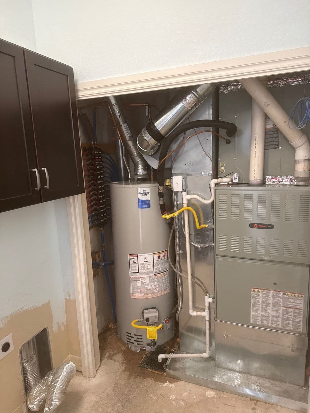 Water heater and HVAC system in a utility closet with exposed pipes and wiring.