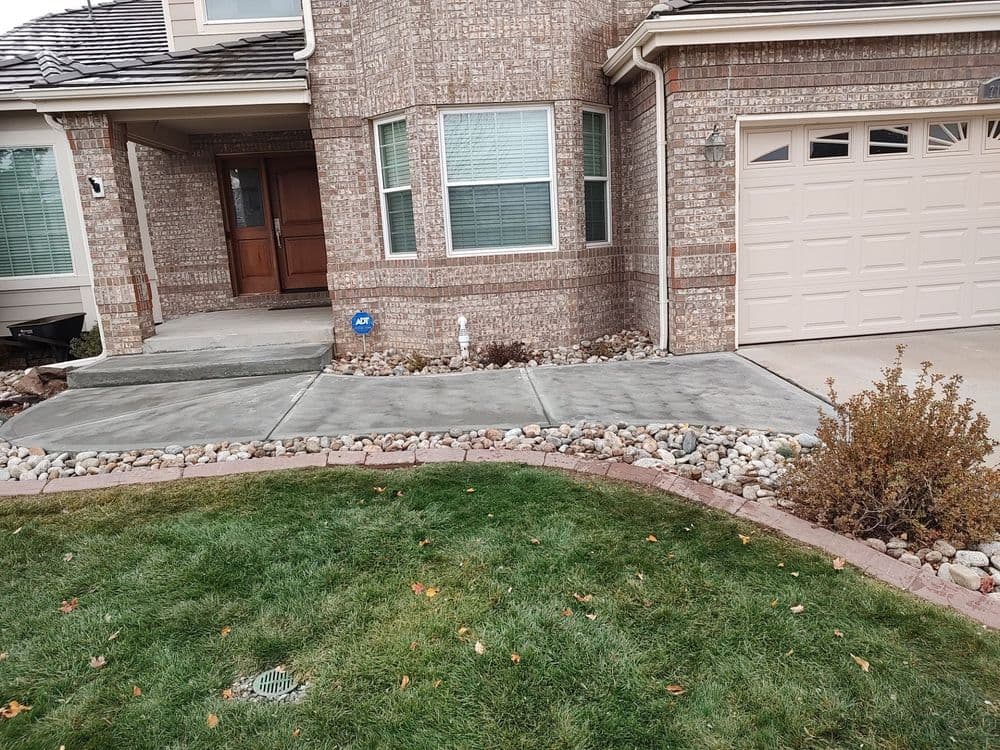 Front entrance of a brick house with a concrete walkway and landscaped garden.