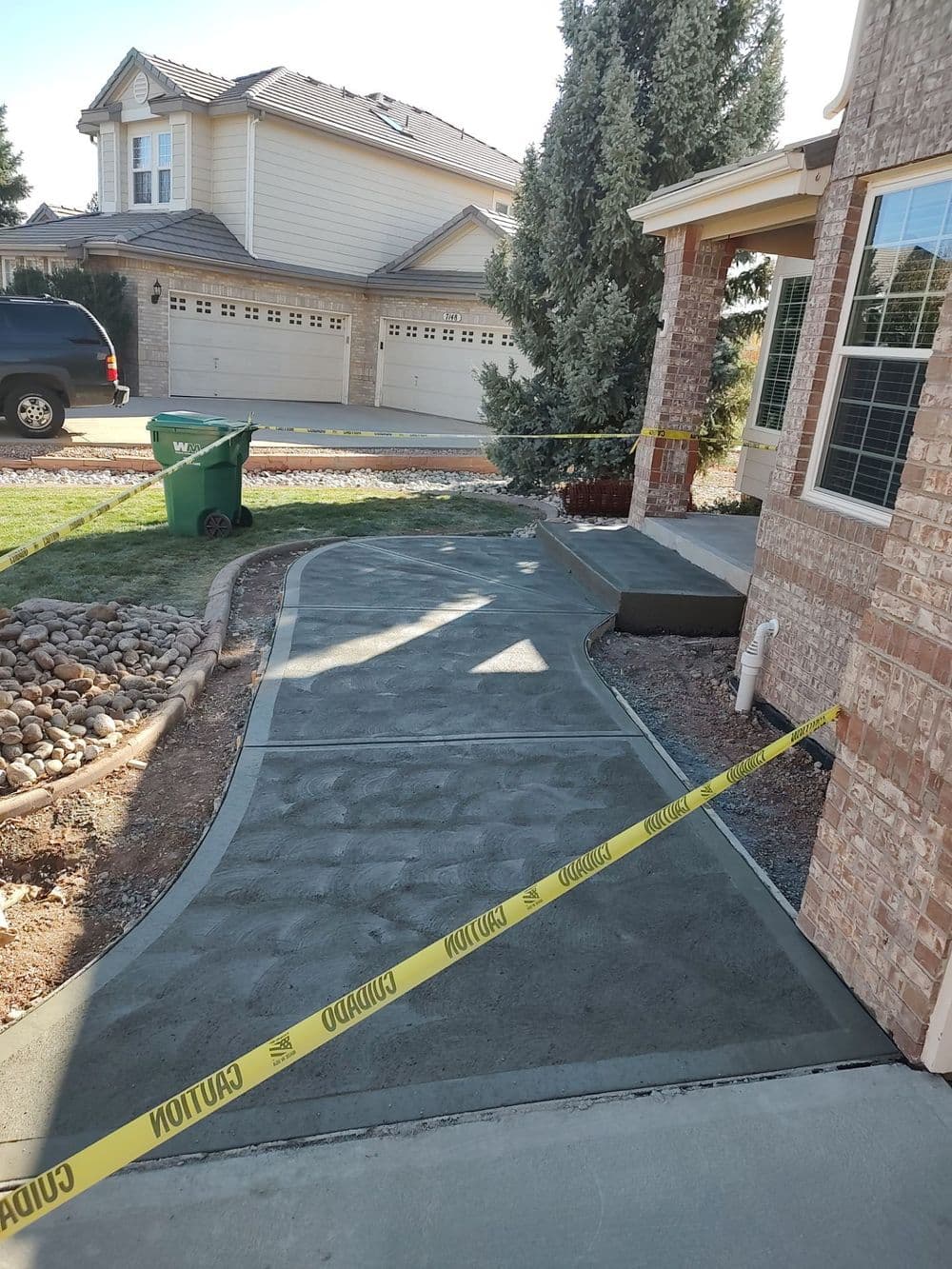 Newly poured concrete sidewalk with caution tape and landscaping in a residential area.