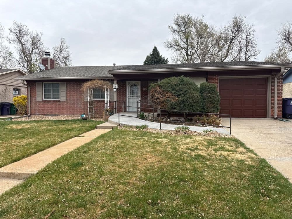 Single-story brick house with a garage, front yard, and landscaped walkway on a cloudy day.