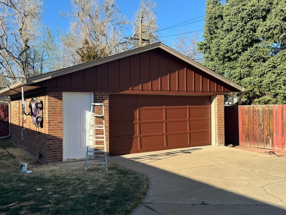 Brown garage with brick exterior, white door, and ladder in a residential setting.