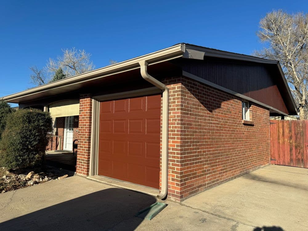Brick garage with brown door and clear blue sky in the background. Residential setting.